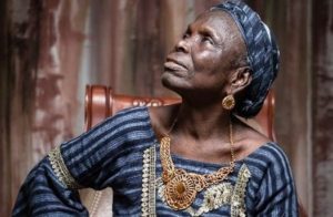 Je côtoie Binta Laly Sow depuis plus de 20 ans maintenant et j’ai rarement vu une personne aussi simple, humble, sociable et généreuse. La simplicité de Binta Laly Sow se lit d’abord sur son style vestimentaire. Toujours en tissu, Wax ou Leppy, cousu sans façon, le cou évasé laissant négligemment découvrir l’épaule et la clavicule qui affleure. Le modèle vintage est même appelé « Binta Laly » dans certains ateliers de couture. Son sac à main à bas coût ne paie pas de mine. Il est souvent effiloché, mais elle n’a que faire ! Binta Laly Sow c’est ensuite une vie simple au milieu des gens ordinaires dans les bas quartiers quand elle est à Conakry ou au village quand elle est en tournée en province. Manger dans un bol de Foutty en groupe, acheter une salade de pomme de terre et laitue au rond-point de la T7 au bord de la route, chez Mariama, mâcher l’autre moitié offerte d’une noix de cola séparée avec les dents, se coincer dans un taxi collectif et même prendre une moto-taxi en pleine nuit, c’est tout Binta Laly Sow. Une simplicité qui peut étonner et même choquer compte tenu de sa notoriété et toute la construction psychologique sur l’opulence supposée des personnes célèbres. Binta Laly est riche mais du cœur, sinon c’est une pauvre hère qui vit au jour le jour en faisant ce qu’elle fait depuis l’âge de 13 ans : chanter. Mais l’indigence de Binta Laly ne l’empêche pas d’être généreuse ; au contraire. Ce bout de femme toujours souriant est un cœur aimant brut de décoffrage. Elle est capable de vider son portefeuille pour n’importe quel « cas social ». Je l’ai vue acheter à manger pour plus aisés qu’elle durant plusieurs années à Sangoyah. Toujours avec le même sourire, toujours avec le même plaisir. Le plus grand amour de Binta Laly va sans conteste à l’endroit de ses enfants « adoptés ». Elle qui n’a pas d’enfants biologiques vivants, a élevé et élève encore de nombreux enfants qui lui ont été « confiés » et qui portent souvent son nom (les fameux homonymes). A la fois une fierté et un fardeau pour elle, confrontée au défi de les héberger, les nourrir, les habiller et les éduquer. Elle n’y arrive pas toujours, évidemment, mais se tue à la tâche pour eux. Cette grande responsabilité de maman-poule l’a poussée à une forme de mendicité tacite. Elle est en quête perpétuelle d’argent et n’hésite pas à revendre des biens précieux pour entretenir ses « poussins » dont certains sont devenus si grands qu’ils ont eux-mêmes de petits-enfants. Mais ils restent dépendants d’elle. Cela permet de mesurer tout le poids de la charge sociale qui pèse sur les épaules frêles de cette grand-mère de 77 ans. Mais paradoxalement, c’est tout ce qui fait le bonheur de Binta Laly Sow ! Elle peut se plaindre d’un moment difficile mais jamais de sa vie entière. Elle est heureuse de ce qu’elle est, de ce qu’elle fait, de son « recevoir-donner », de sa vie ordinaire. Binta Laly agit telle une "passeuse" de l’entraide. Elle demande pour donner. Mais jusqu’à quand pourrait-elle faire ça ? Si Abdoulaye Sadio Diallo et moi-même avons initié le projet « Un toit pour Binta » en sa faveur, ce n’est point pour l’arrêter de faire ce qui lui plait. C’est plutôt pour l’aider à le faire de façon plus organisée avec moins de contrainte et de prise de risques. Car son bonheur est très précaire. Nous avons, en effet, senti depuis quelques années le piège de l’âge en train de se refermer sur elle petit à petit. Alerte et en bonne santé, elle ne s’en rend pas compte. C’est une personne vulnérable, car si aujourd’hui si elle s’arrêtait de chanter et de faire sa quête, elle tomberait inévitablement dans la dépendance. Et à ce moment-là, sa simplicité et sa générosité risquent d’être considérées par une opinion intolérante aux idées préconçues comme de la « naïveté », voire une « malédiction » de sa part. Nous voulons lui éviter cela. Éviter un tel sort à une icône nationale dont la contribution au rayonnement de la culture traditionnelle guinéenne est inestimable. Épargner une telle gêne à la Guinée. Notre projet répond à cette préoccupation : lui trouver une source de revenus durables pour qu’elle puisse prendre sa retraite quand elle le voudra (ou quand celle-ci s’imposera) en toute sécurité. Aidez-nous à l’aider. Contact : 611 20 63 98 ; bintalalysow@gmail.com